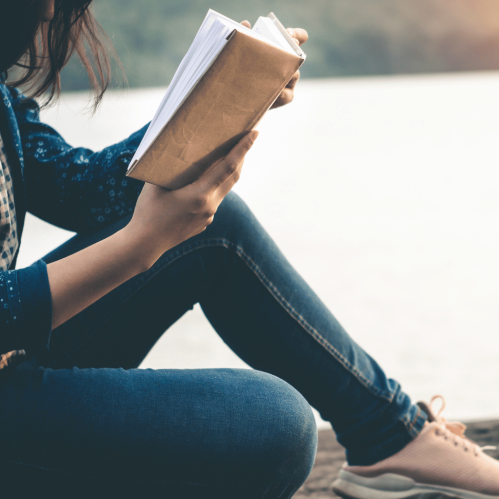 Woman sitting by the water reading a book