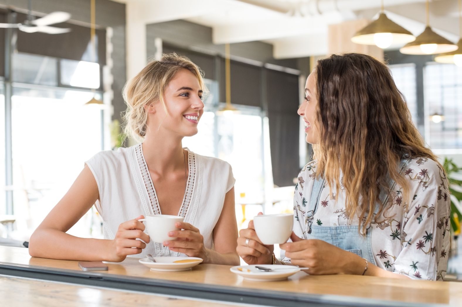 Two young women sit at a coffee bar discussing their work