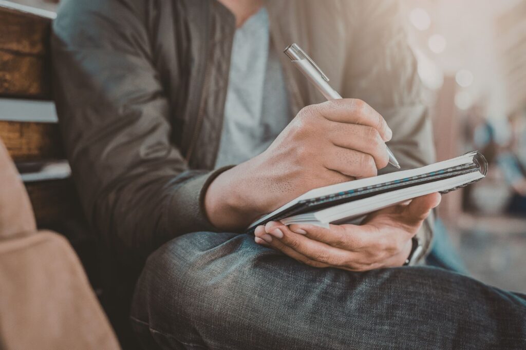 Man writing is book by hand, sitting on a bench