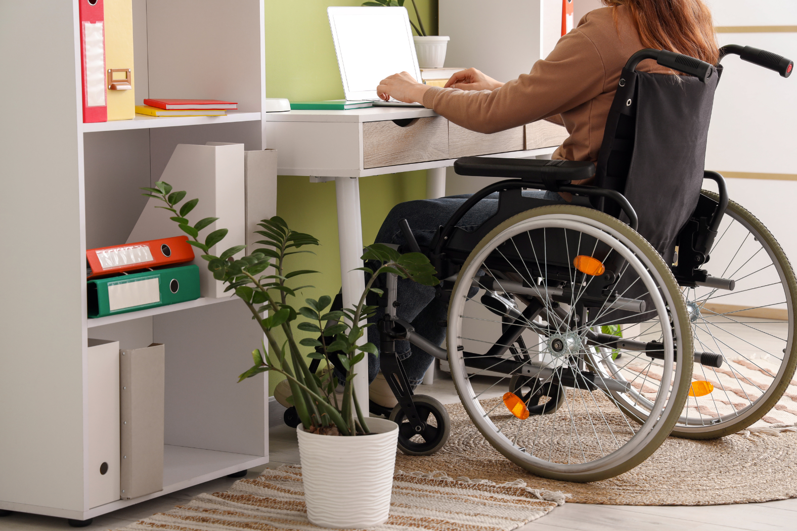 Woman in a wheelchair sits at her desk, working on her laptop