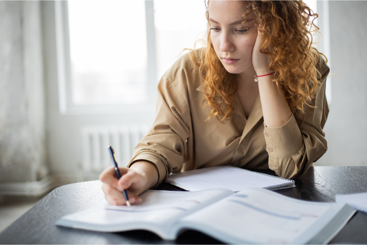 Young woman sits with head in her hands as she writes.
