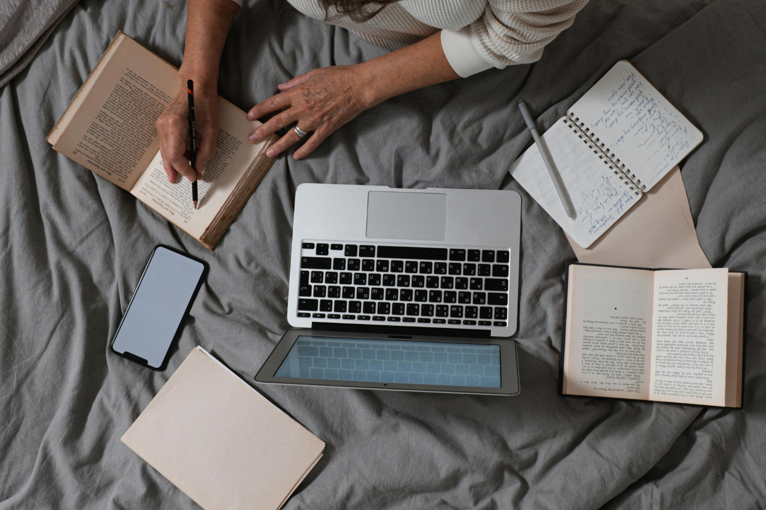 A woman writing on a notepad, with books, laptop, and books surrounding her.