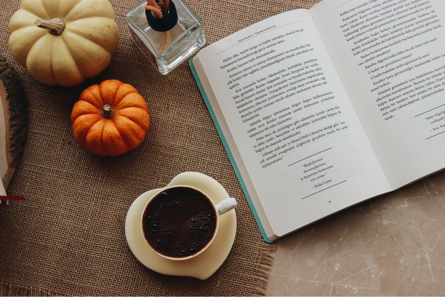 Open book, coffee mug, and pumpkins sit on a table top.